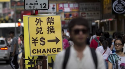Viandantes junto al cartel de una oficina de intercambio divisas en Hong Kong (China).