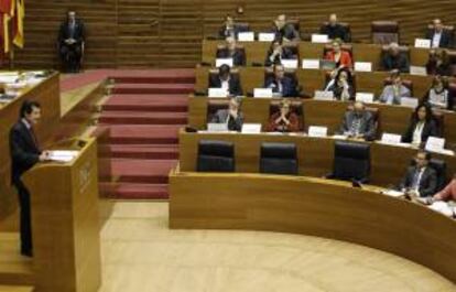 El vicepresidente de la Generalitat, José Císcar (I), informa en el Pleno de Les Corts sobre la decisión de cerrar Radiotelevisión Valenciana (RTVV), mientras los diputados socialistas muestran carteles donde se puede leer "RTVV no es tanca".