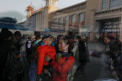 Una mujer con un bebé en brazos se refleja en la ventana de la estación de tren de Pekín (China), el 1 de febrero de 2018.