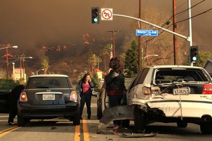 Unas personas se piden la documentación de sus vehículos tras el accidente de coche que han sufrido, al fondo el monte San Gabriel envuelto en llamas visto desde Glendora, (California).
