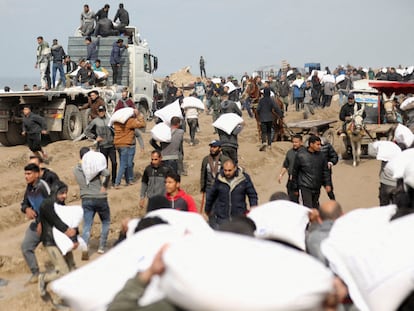Palestinians carry bags of flour they grabbed from an aid truck near an Israeli checkpoint, February 19, 2024.