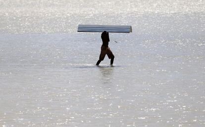 Un hombre carga una plancha de zinc al cruzar un r&iacute;o, cuyo puente fue destruido durante el paso del hurac&aacute;n Matthew.