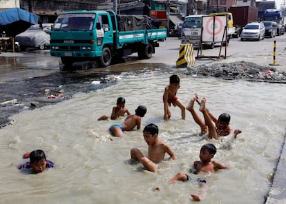 Niños se dan un baño en una carretera en reparación en el distrito de Tondó (Filipinas).