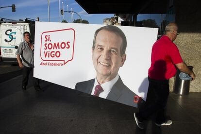 Dos operarios trasladan un cartel con la imagen del alcalde y candidato del PSOE a la reelección de Vigo, Abel Caballero, a la sede del partido antes de la rueda de prensa.