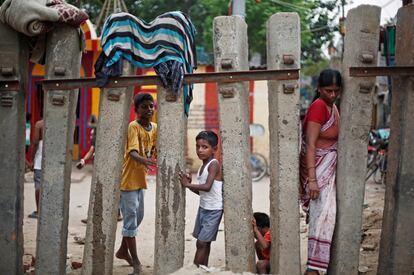 Los niños juegan mientras una mujer cruza una valla de ferrocarril en una zona de tugurios, en Nueva Delhi, (India).