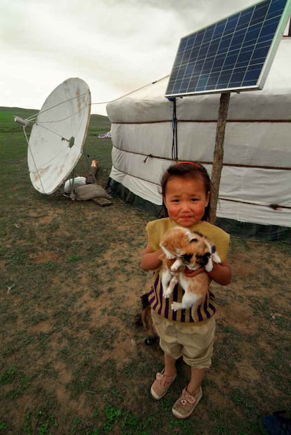 La hija menor de Oyunbileg, nómada mongol, posa con dos gatos frente a la placa solar y la antena que les permite recibir televisión por satélite.