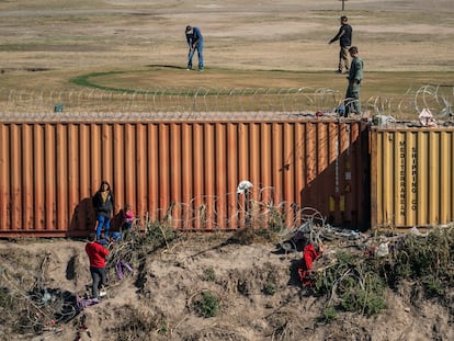 Un pequeño grupo de migrantes se topa con un muro de contenedores a su llegada a Eagle Pass, en Texas. Del lado estadounidense, un grupo de hombres juegan golf.