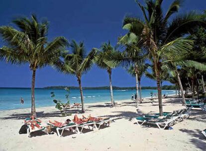 Turistas bajo palmeras en Bloody Bay Beach, una de las playas más largas de Jamaica