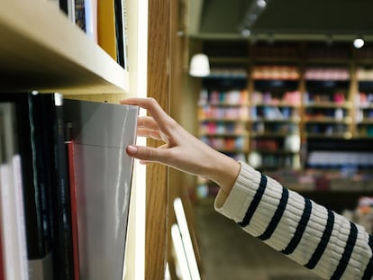 Una joven coge un libro en una biblioteca.