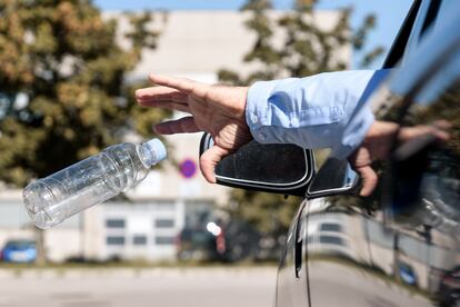 Un hombre arroja una botella de plástico vacía por la ventanilla de su coche.