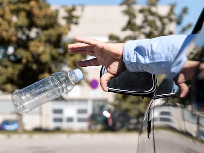 Un hombre arroja una botella de plástico vacía por la ventanilla de su coche.