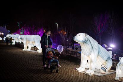 Un padre con su hijo en un carrito contempla una de las esculturas de osos iluminadas. 