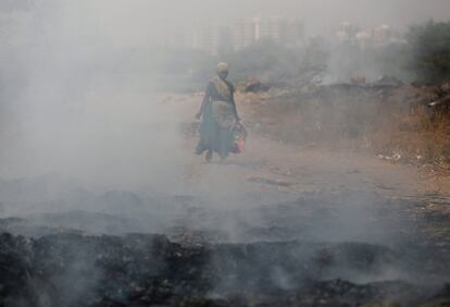 Un trapero que lleva material reciclable es vistro a través del humo brota de la basura que se quema en un vertedero en las afueras de Ahmedabad, (India).
