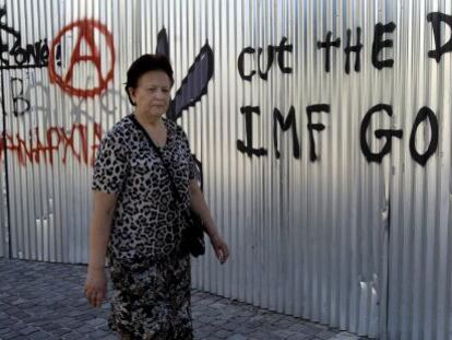 Una mujer camina junto a un grafiti en el que se puede leer &quot;FMI vete a casa, corta la deuda&quot; en Atenas.