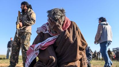 Um militante curdo armado protege um homem pensativo que acaba de escapar de Baghuz em 1º de março na província de Deir Ezzor.