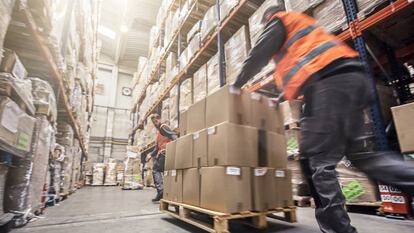 Dos trabajadores del sector logístico trasladan un palé cargado de cajas.