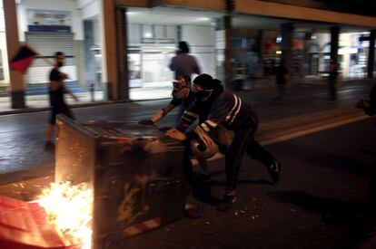 Dos manifestantes empujan un cubo de basura en llamas por una calle de Atenas.