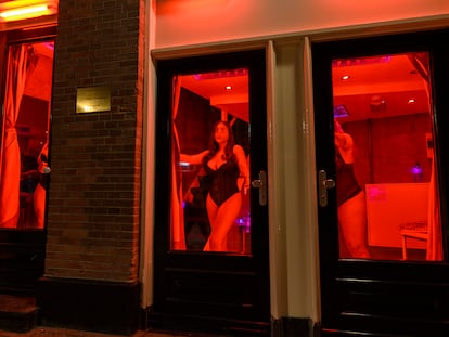 Women stand in the window of an establishment in Amsterdam’s Red Light District