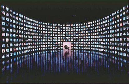 Una persona sentada frente a 500 aparatos de televisión conectados a 500 diferentes canales.