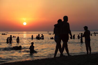 Bañistas y paseantes disfrutan de un atardecer en una playa de Cava D’Aliga, en Sicilia (Italia).