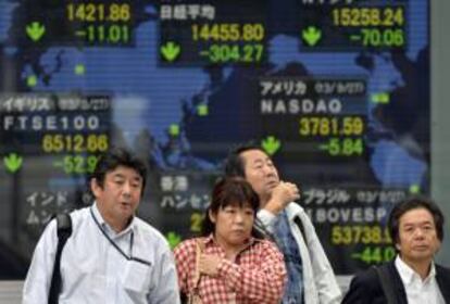 Japoneses pasan por delante de una pantalla con los resultados de la bolsa de Tokio.