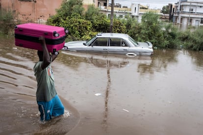 Un hombre traslada una maleta frente a un coche sumergido por las inundaciones en Keur Massar (Dakar).