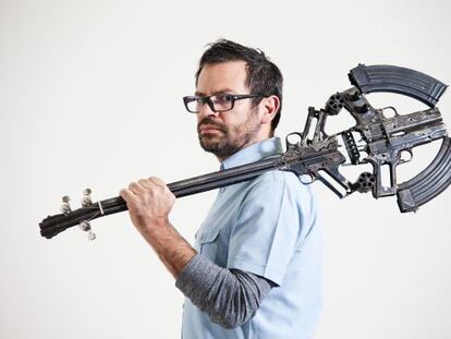 El artista Pedro Reyes sostiene una guitarra hecha con armas.