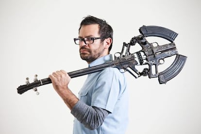 El artista Pedro Reyes sostiene una guitarra hecha con armas.