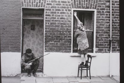 Dos mundos sucediendo a la vez: un soldado con su arma en un portal mientras una mujer limpia las ventanas en Belfast en 1973.