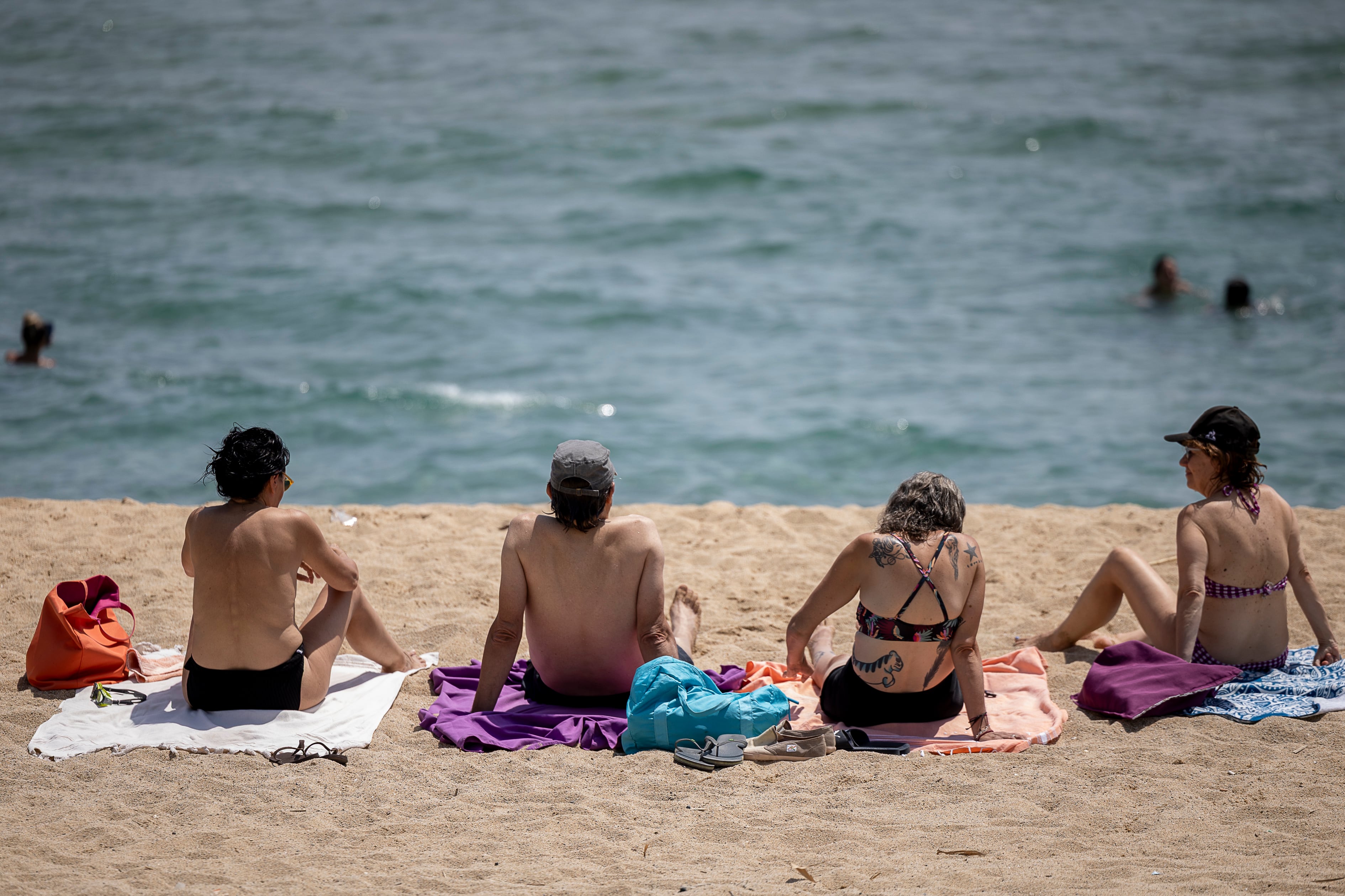 Cuatro personas toman el sol en Playa de les Barques de Montgat, en Barcelona, el 31 de julio de 2026. De ellas, una hace toples.