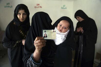 Una mujer completamente cubierta, con su bebé en brazos, enseña su tarjeta de registro electoral.