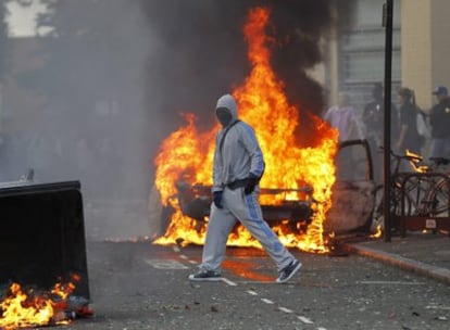 Un hombre encapuchado cruza una calle cortada por contenedores ardiendo, en el conflictivo barrio de Hackney, al este de Londres