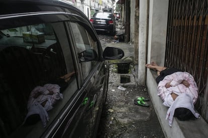 Un vagabundo se refleja en la ventanas de un vehículo mientras duerme en la puerta de una tienda en Kuala Lumpur, Malasai, el 21 de mayo de 2016.