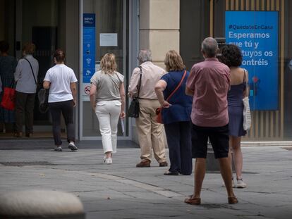 Varias personas esperan su turno en la calle para entrar en un banco en Sevilla, este lunes.