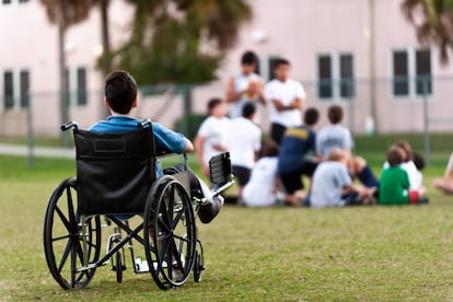 Un adolescente en silla de ruedas observa a sus compañeros jugando en el parque mientras le excluyen.