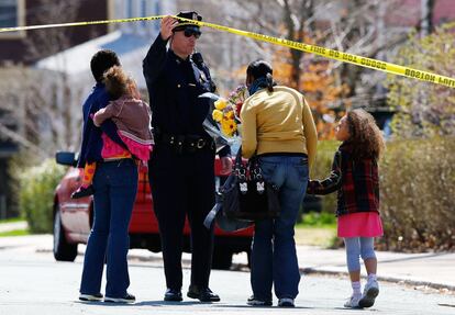 Un agente de policía de Boston, levanta la cinta amarilla para que una familia pueda llevar unas flores a casa de Richard, un niño de ocho años muerto en el atentado del Maratón de Boston (EE UU).