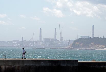 Un hombre camina sobre un muro del rompeolas en el puerto pesquero de Ukedo, cerca de la central nuclear de Fukushima (al fondo), en Namie, este jueves.