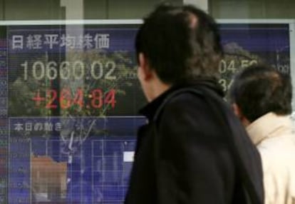 Un par de viandantes pasn delante de una pantalla que muestra información bursátil de hoy en el centro de Tokio (Japón).