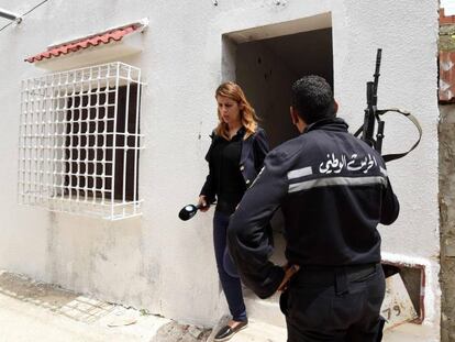 Un agente tunecino junto a una periodista que abandona la casa en la que dos yihadistas han muerto este mi&eacute;rcoles. 