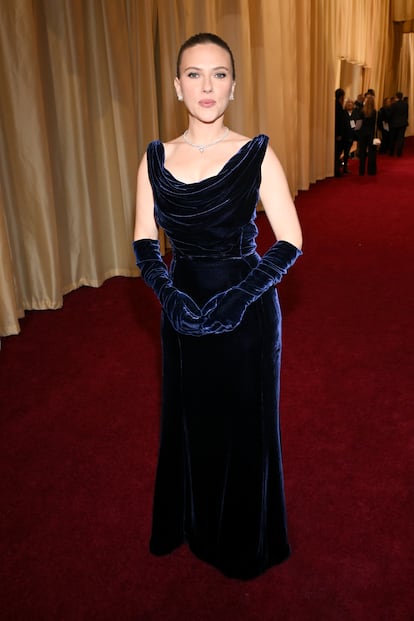 2025. Scarlett Johansson deslumbró en la alfombra roja con un vestido vintage de terciopelo azul marino de Thierry Mugler, perteneciente a la colección Otoño-Invierno 1999/2000 "Les Méduses". El diseño presentaba un escote drapeado sin mangas y una silueta columna que realzaba su figura. Completó el look con guantes largos a juego y joyas de De Beers, incluyendo un collar de diamantes y pendientes de botón.