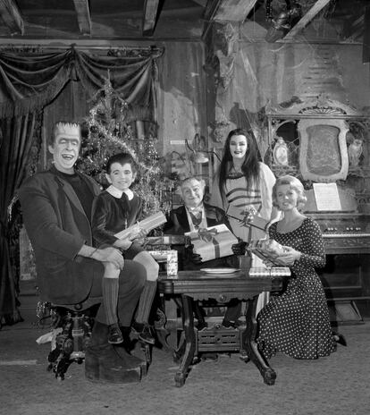 El reparto de la serie de televisión 'Los Monster' sentado alrededor de una mesa cargados de regalos de Navidad (1963).