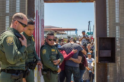 US border guards watch as families from both sides of the fence greet each other.