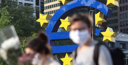 Personas con mascarilla pasan delante del símbolo del euro que preside la sede del Banco Central Europeo en Fráncfort.