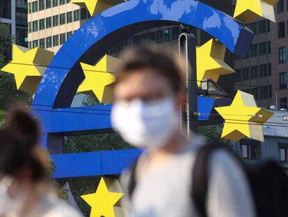 Personas con mascarilla pasan delante del símbolo del euro que preside la sede del Banco Central Europeo en Fráncfort.