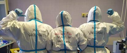 Tres trabajadores del Hospital Santo Spirito señalan sus trajes protectores mostrando sus nombres y la fecha de vacunación contra el coronavirus.