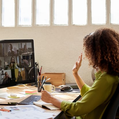 Barcelona. Female freelancer waving hand with colleagues while attending video call at home office. Businesswoman with coworkers planning strategy. They are discussing together.