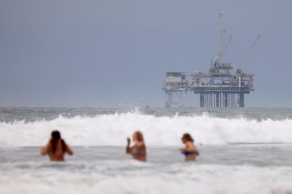 Un grupo de personas se baña en una playa de California, con una planta petrolífera detrás.