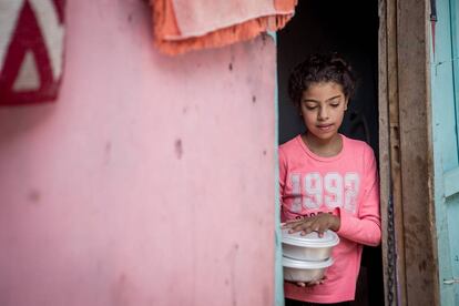 Natalia Macario, de siete años, recibe un plato de comida. La niña y su hermano siguen las clases desde casa por teléfono móvil.