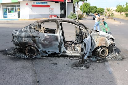 Una mujer y un niño caminan junto a un coche quemado en medio de la violencia entre cárteles, en Culiacán.