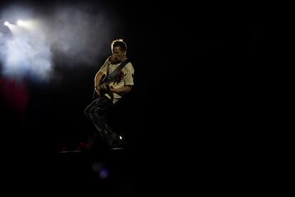 Las luces blancas del escenario principal apuntan directamente a Bellamy mientras toca la guitarra.